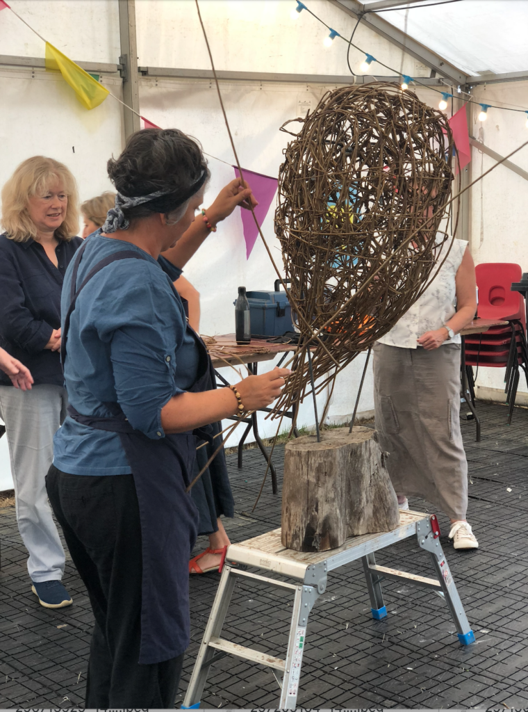 Vik from Weird Sticks demonstrating willow weaving technique to create a community owl sculpture during the Crediton Heart project