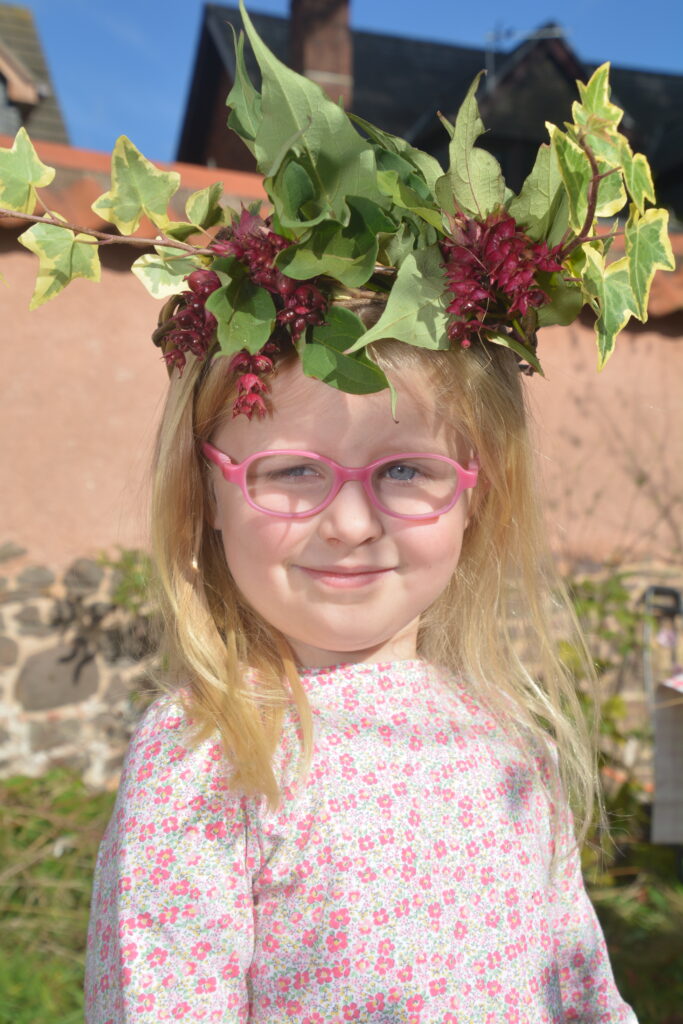 Child wears willow harvest crown heavily decorated with leaves and flowers