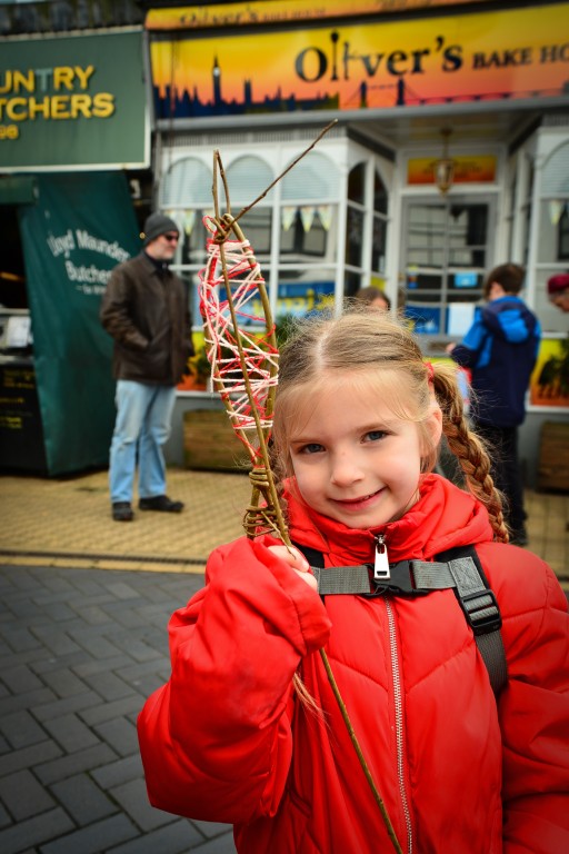 Smiling child holding up finished willow and wool fish on a willow fishing rod at Playing in the Streets Easter 2023 in Brixham