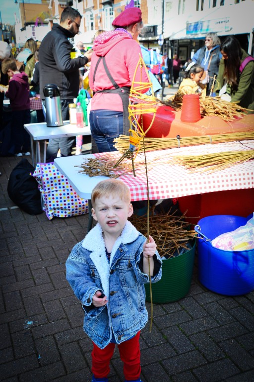 Child holding up finished willow and wool fish on a willow fishing rod at Playing in the Streets Easter 2023 in Paignton