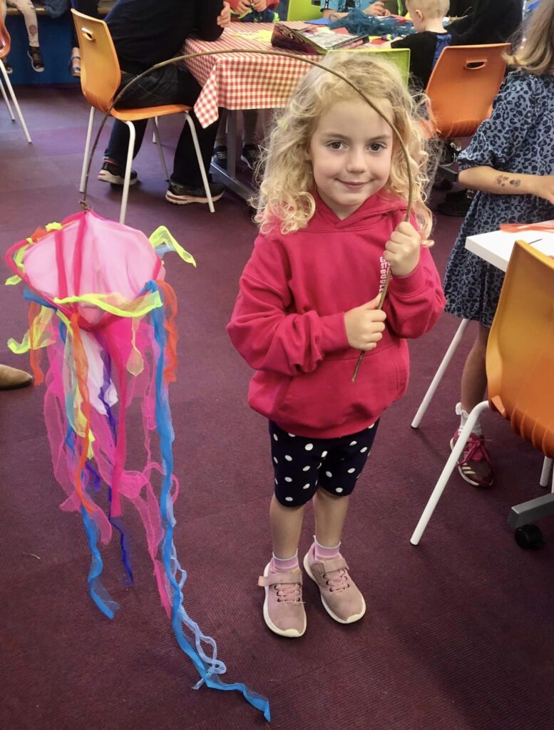 Child displaying their decorated parade jellyfish creation at the Weird Sticks family workshops at Exmouth Library
