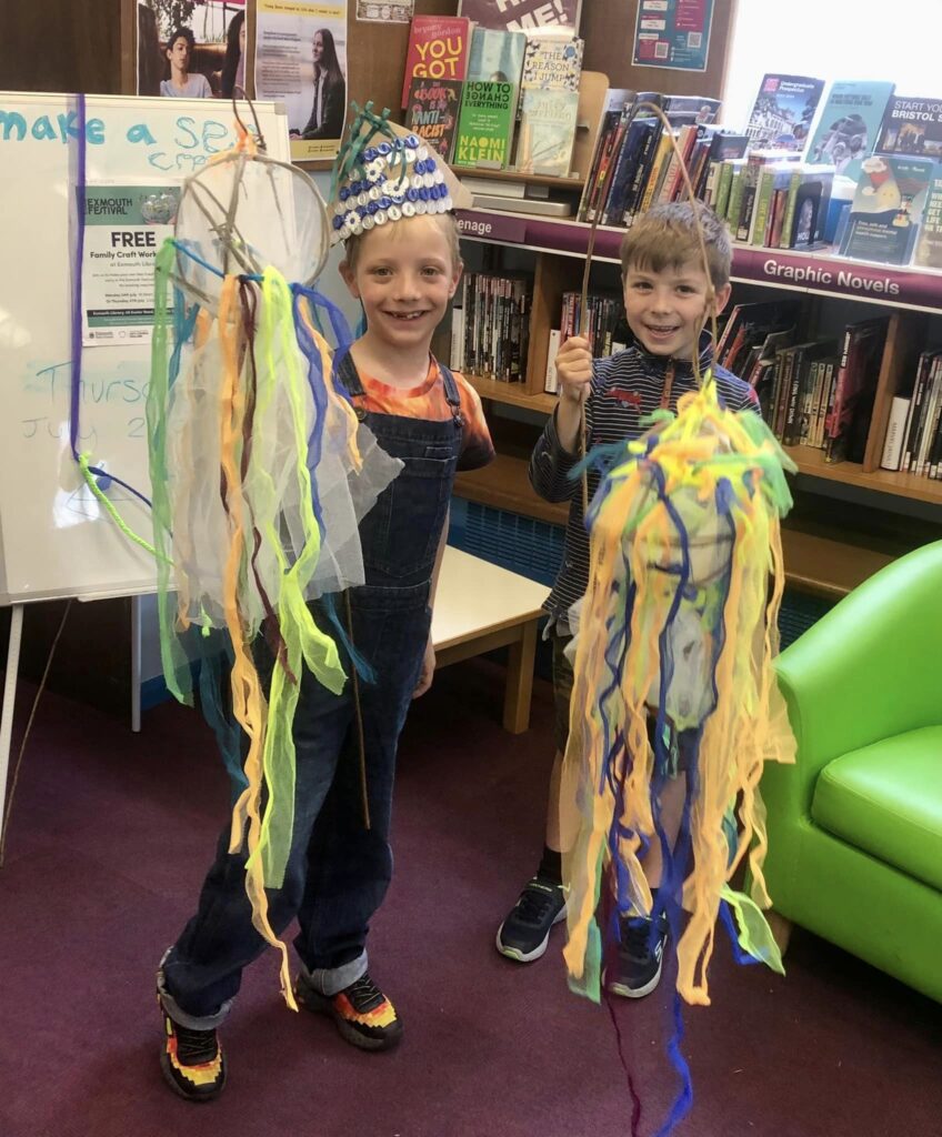 Two young children displaying their sea creature parade creations at the Weird Sticks family workshops at Exmouth Library