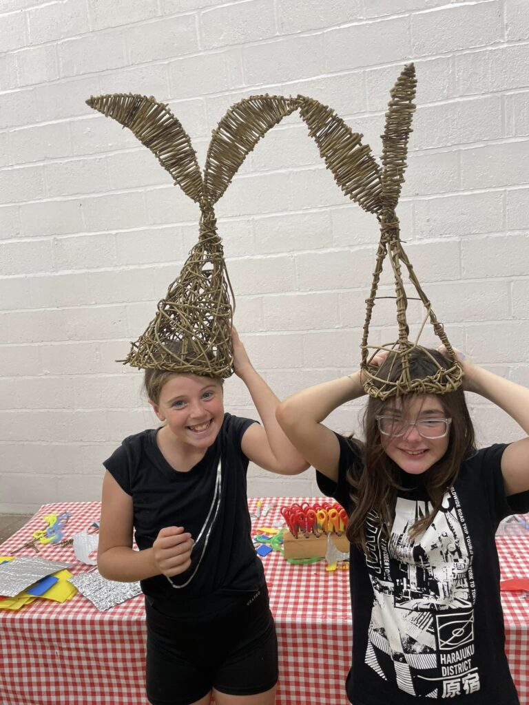 Two children wearing willow fish tail parade hats created with Weird Sticks at Play Torbay
