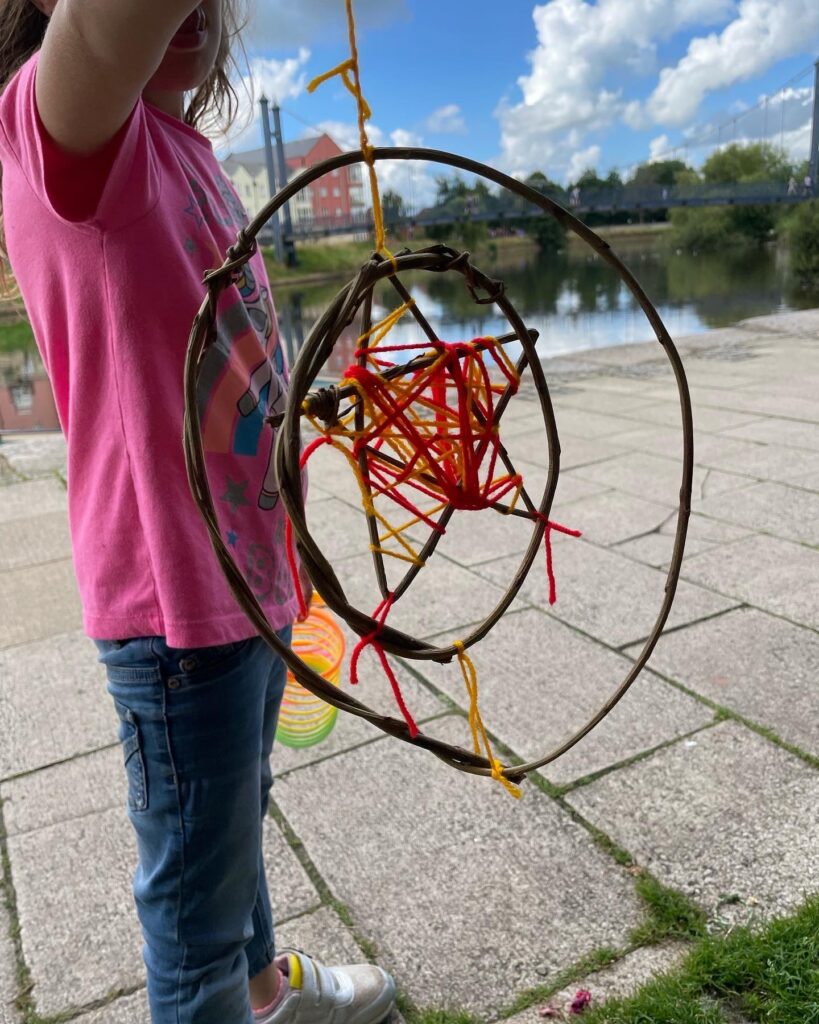 Child displaying their willow and wool spinning sun at the Weird Sticks workshop, Exeter Quay
