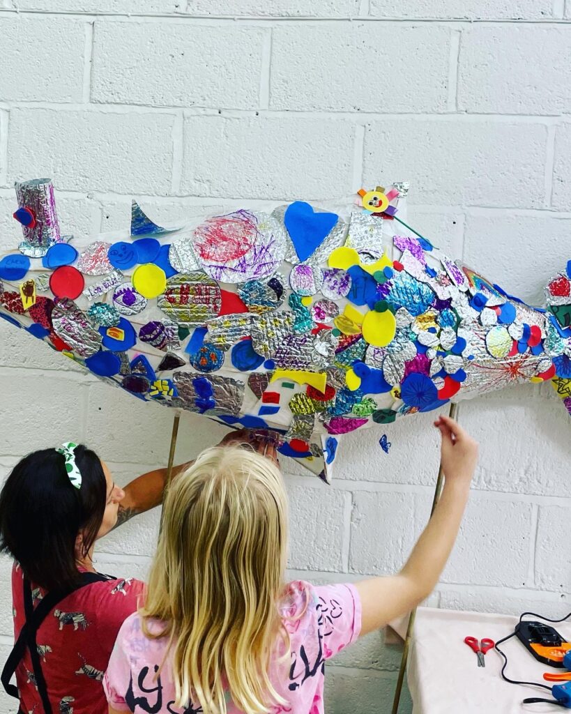 Hannah from Weird Sticks helping a child to decorate giant fish parade puppet at Play Torbay