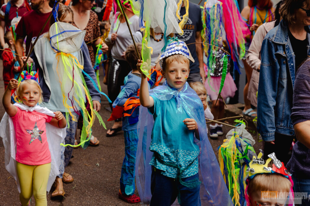 Children and families carrying their sea creature creations and costumes made with Weird Sticks in the Exmouth Festival samba parade
