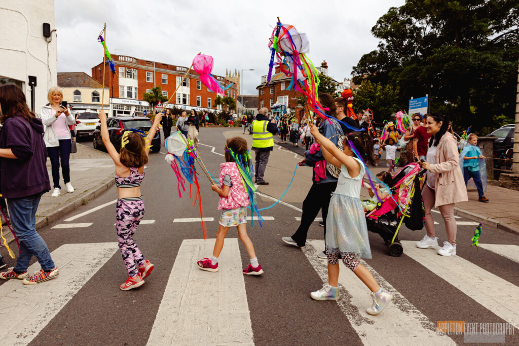 Children and families carrying their sea creature creations and costumes made with Weird Sticks in the Exmouth Festival samba parade
