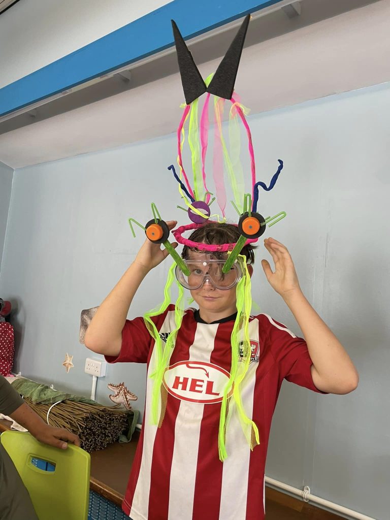 Child wearing their space-themed creations at the Weird Sticks workshop at Exmouth Library for Exmouth Festival 2024