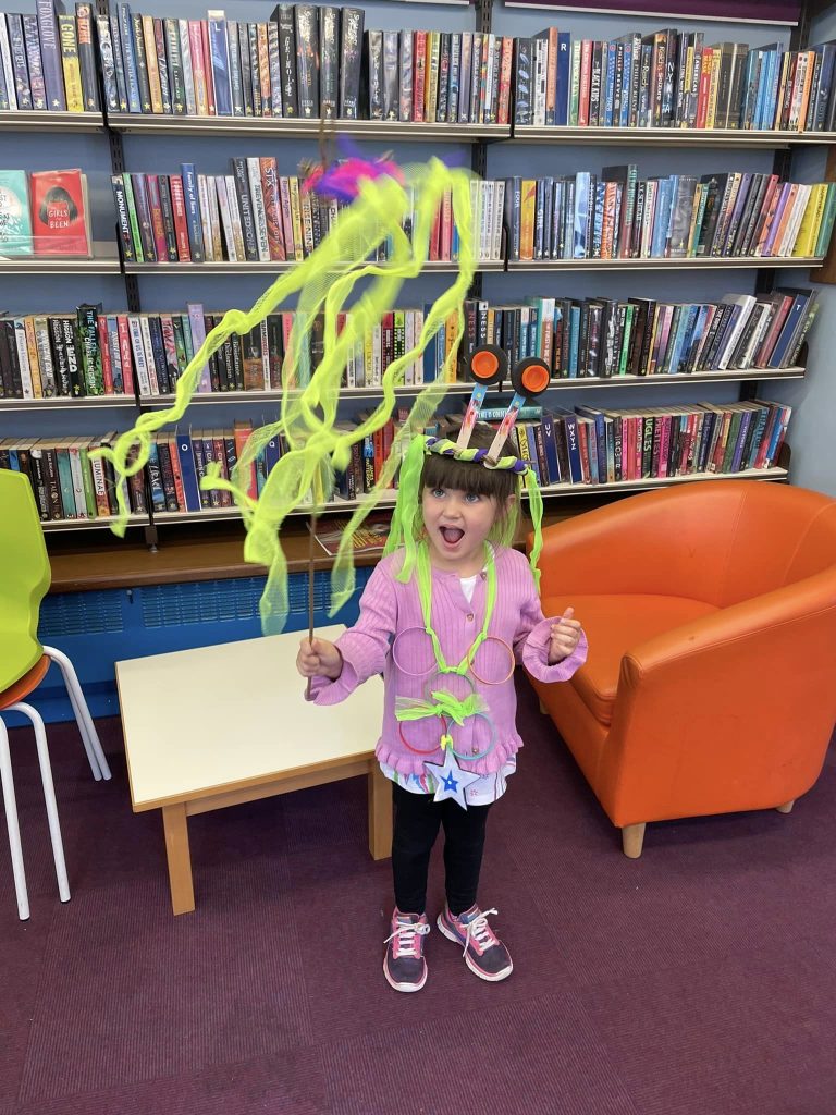 Child wearing their space-themed creations at the Weird Sticks workshop at Exmouth Library for Exmouth Festival 2024