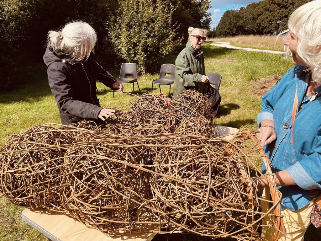 Participants weaving community ammonite sculpture created with Weird Sticks at A La Ronde