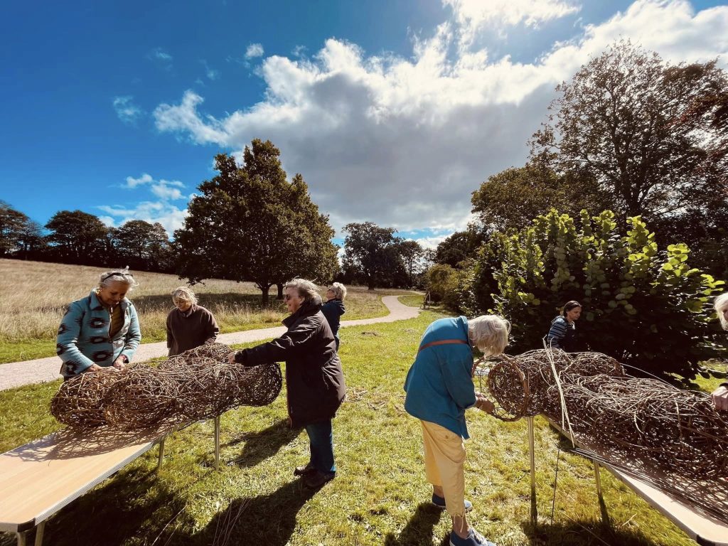 Participants weaving community ammonite sculpture created with Weird Sticks at A La Ronde