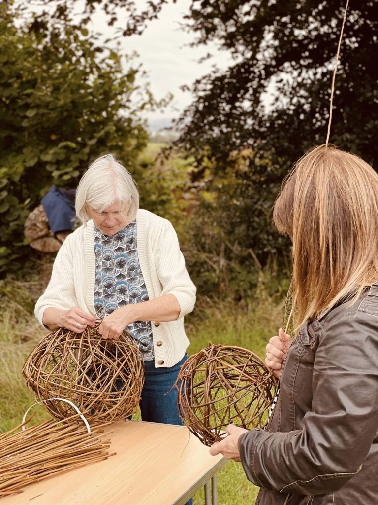 Participants weaving willow spheres for community ammonite sculpture created with Weird Sticks at A La Ronde